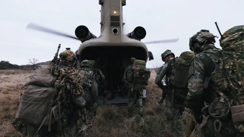 Militairen in het veld lopen via de laadklep een Chinook met draaiende rotors in.