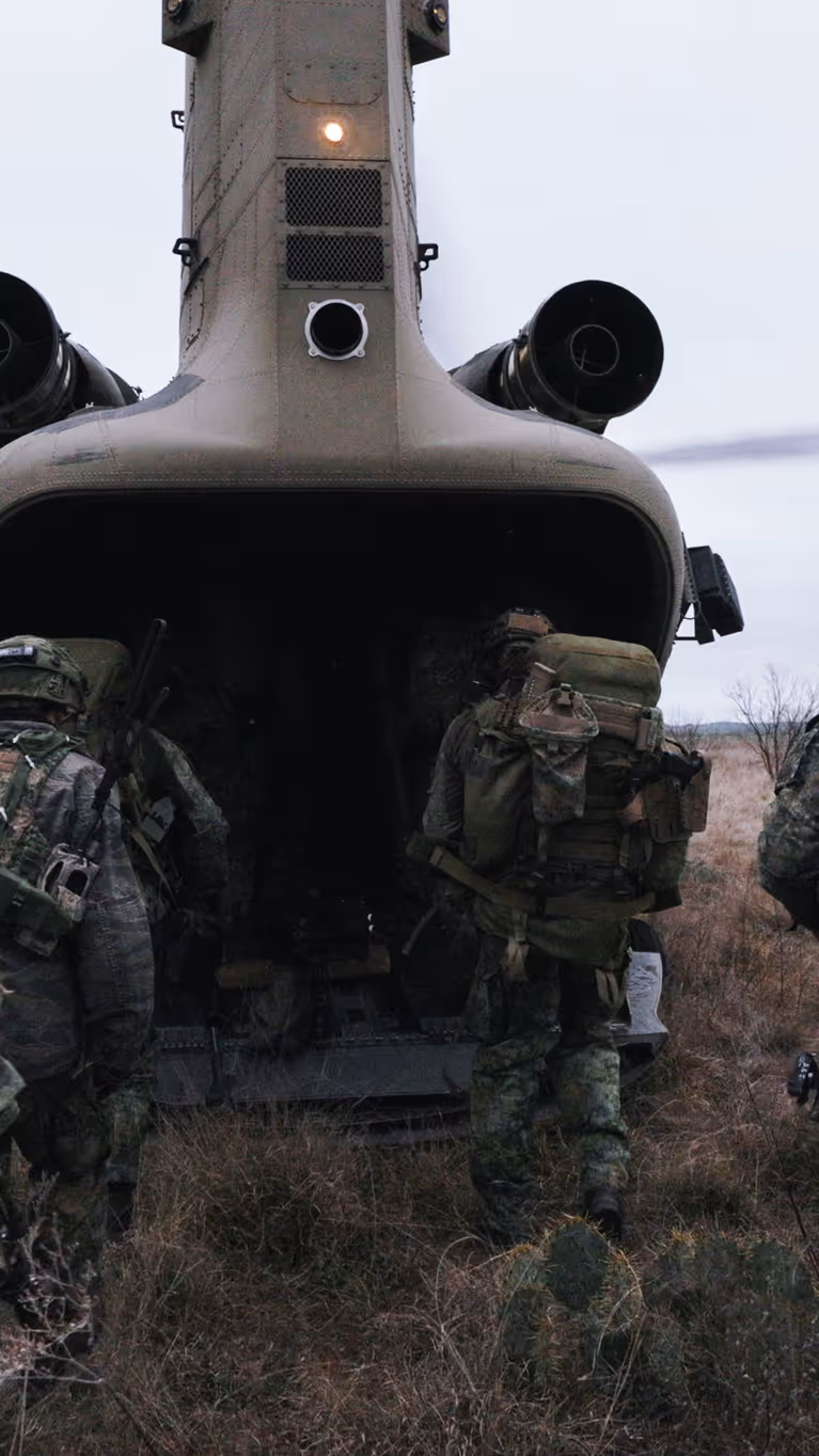 Militairen in het veld lopen via de laadklep een Chinook met draaiende rotors in.