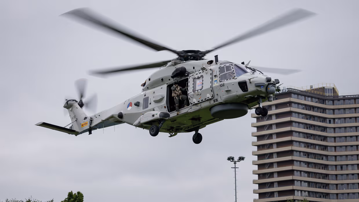 Een Chinook stijgt op boven een veld, met aan een lange kabel de Nederlandse vlag