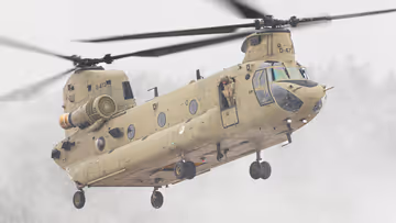 Een helikopter maakt een landing op een wit veld. Rechts met een paar pakketten onder zich. 