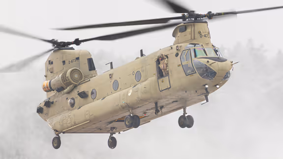 Een helikopter maakt een landing op een wit veld. Rechts met een paar pakketten onder zich. 