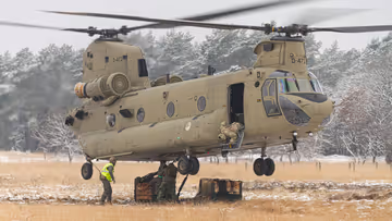 Een helikopter maakt een landing op een wit veld. Rechts met een paar pakketten onder zich. 