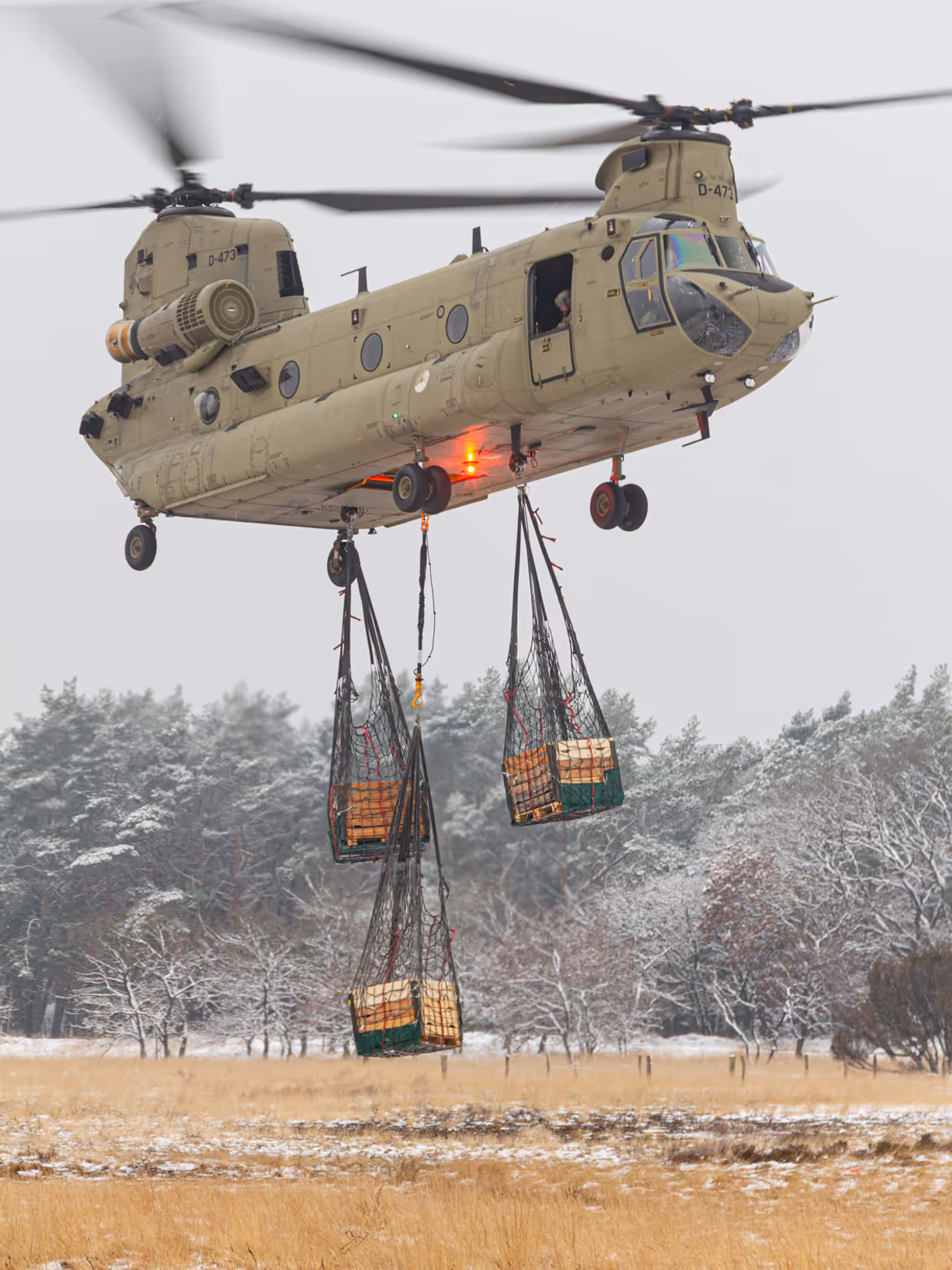 Een helikopter maakt een landing op een wit veld. Rechts met een paar pakketten onder zich. 