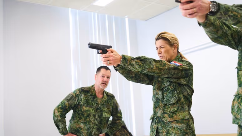 Alt-tekst: Koningin Maxima richt een wapen. 