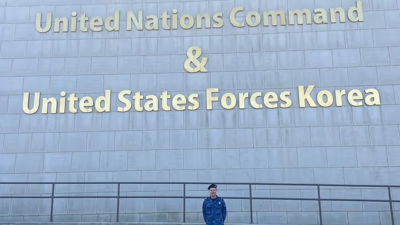  Leon Diender voor een grijs gebouw, met daarop de tekst ‘Hoofdkwartier United Nations Command and United States Forces Korea’.