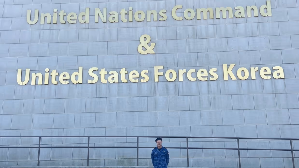  Leon Diender voor een grijs gebouw, met daarop de tekst ‘Hoofdkwartier United Nations Command and United States Forces Korea’.