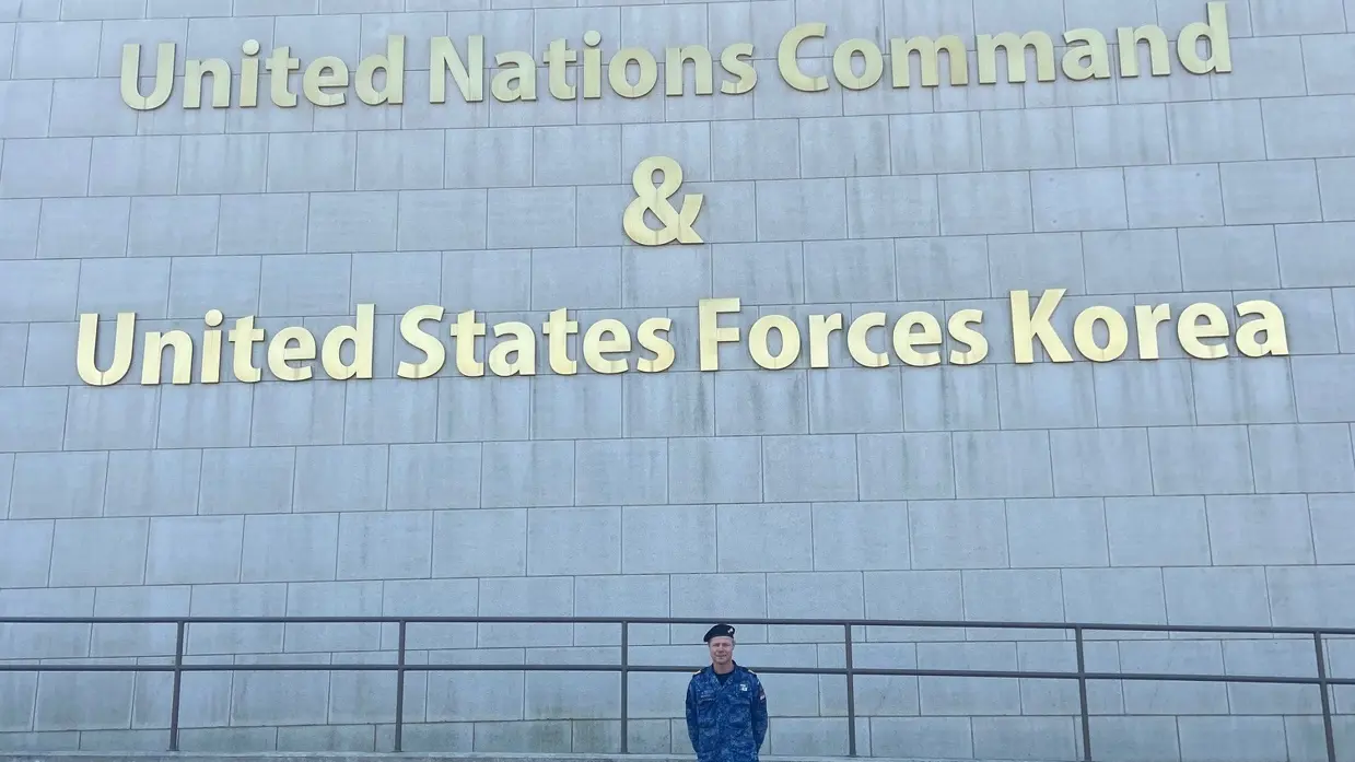  Leon Diender voor een grijs gebouw, met daarop de tekst ‘Hoofdkwartier United Nations Command and United States Forces Korea’.