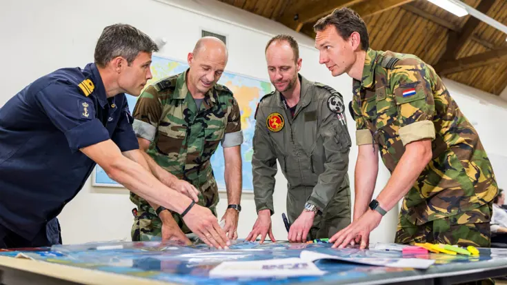 4 militairen praten staand bij een tafel.