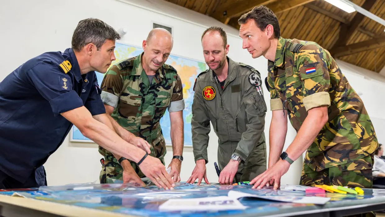 4 militairen praten staand bij een tafel.