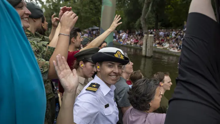 Een militair lacht naar de camera terwijl ze op een boot staat.