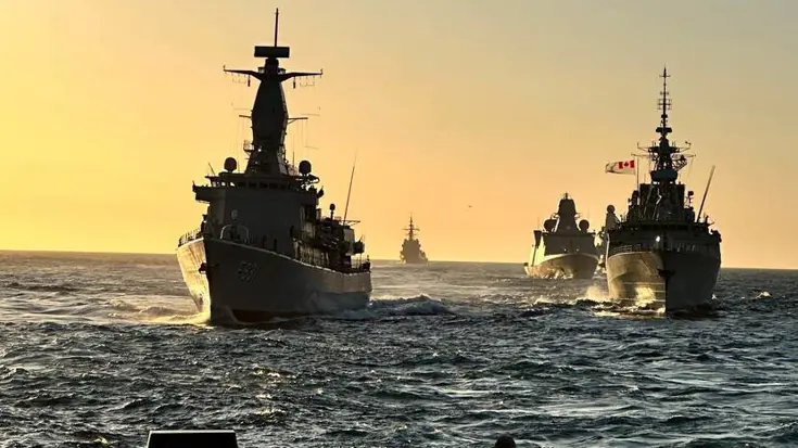 Varende militaire schepen met pastelkleurige lucht als achtergrond.