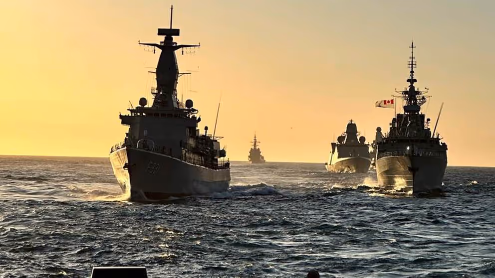 Marineschepen varen achter elkaar op zee.