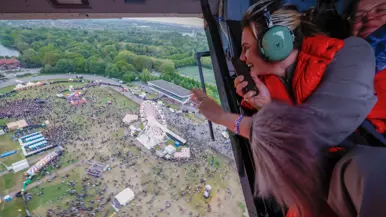  Zangeres Maan zwaait door de open deur van een vliegende heli naar publiek op het festivalterrein onder hen.