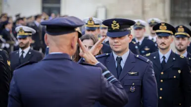Steur en een leerling-vlieger met wing brengen elkaar de militaire groet. Achter de leerling staat een groep militairen opgesteld uit verschillende landen. 