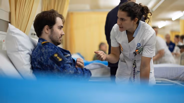 Militair in ziekenhuis bed. Verpleegster praat met hem.