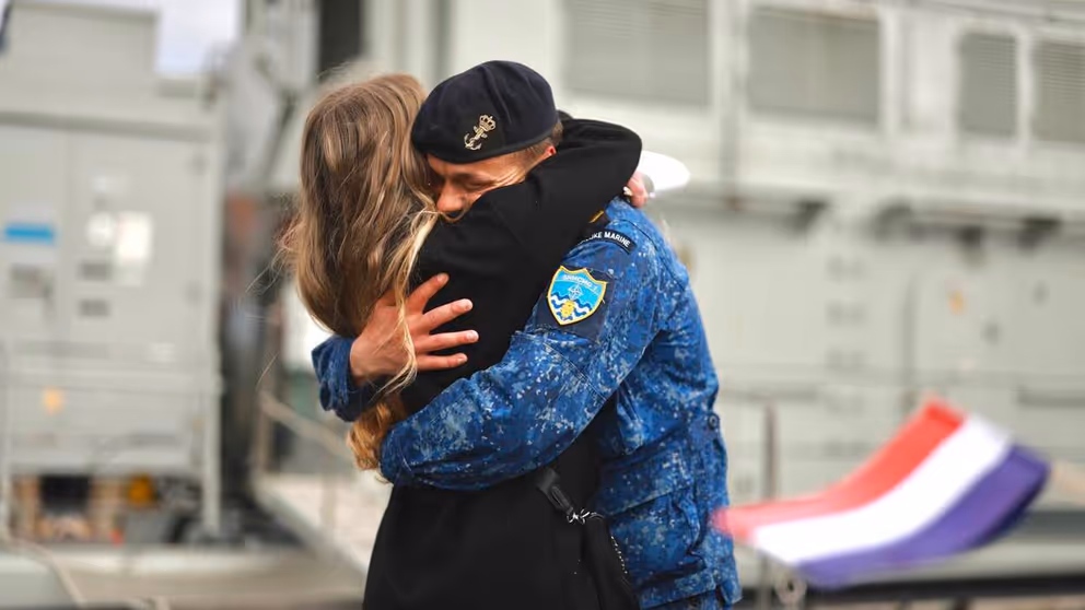 Marineman omhelst vrouw. Op de voorgrond Nederlands vlaggetje.