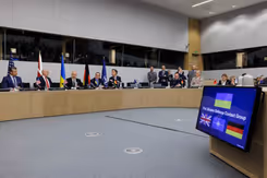 Zaal met sprekers van de 31e Ukrain Defence Contact Group. Op de voorgrond is veel grijze vloer zichtbaar.