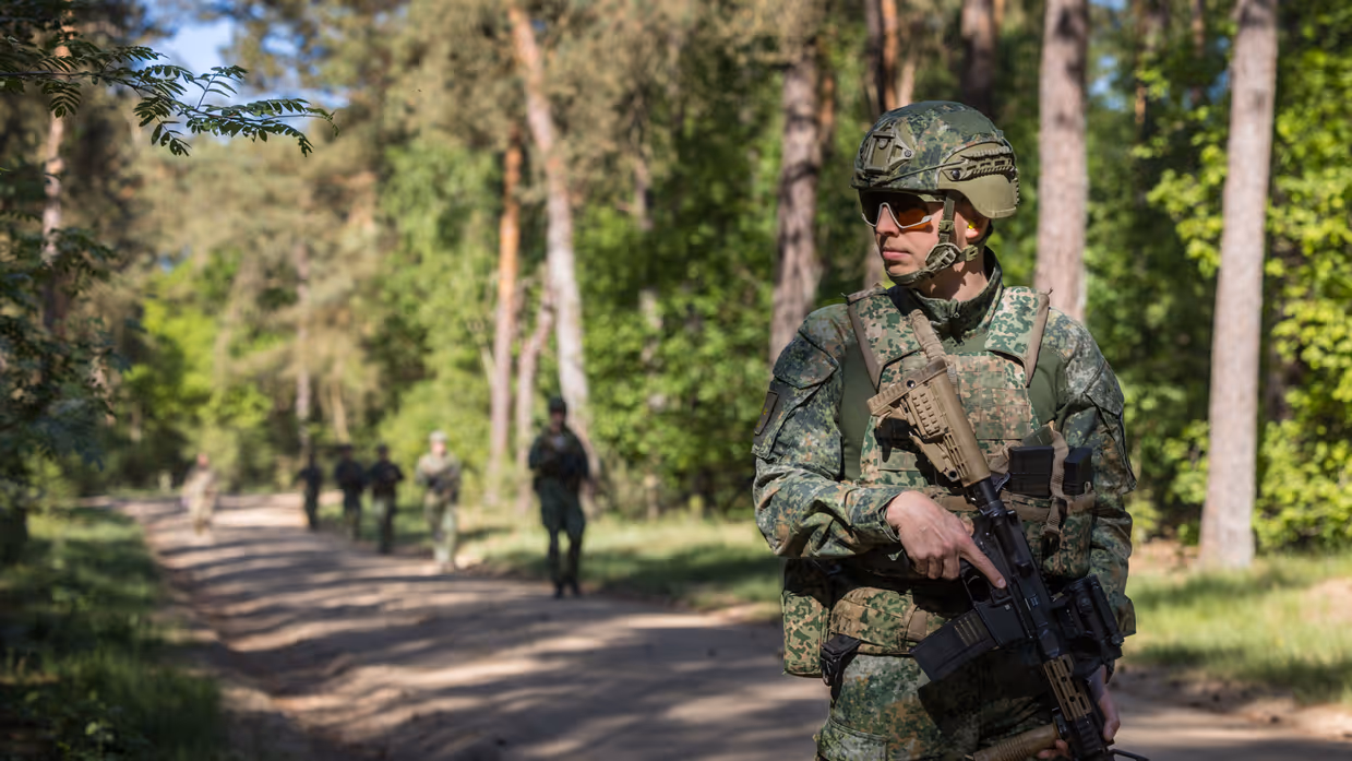 Marechaussee in groen uniform, met een lang wapen in de hand.