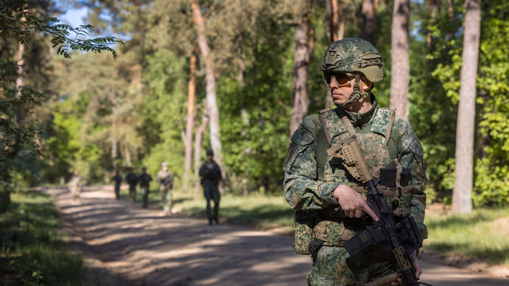 Marechaussee in groen uniform, met een lang wapen in de hand.
