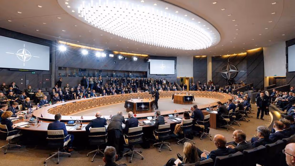 Ovale zaal met sprekers in pak uit uiteenlopende landen.