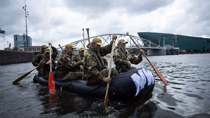 De deelnemers roeien door de grachten van Amsterdam. 