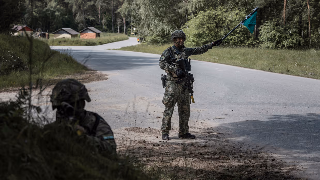 Marechaussee in groen tenue met een groene vlag in zijn hand met op de voorgrond een andere militair.