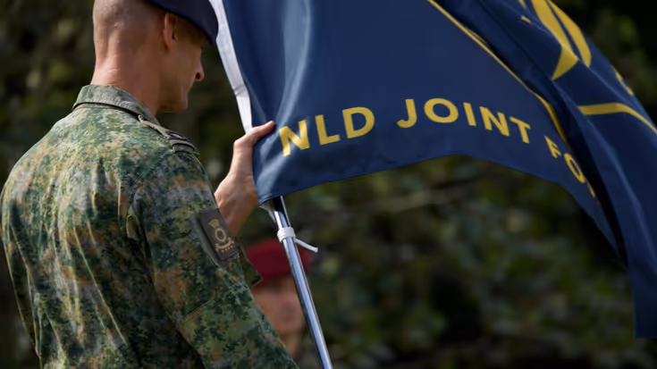 Een militair houdt de vlag van JFC vast.