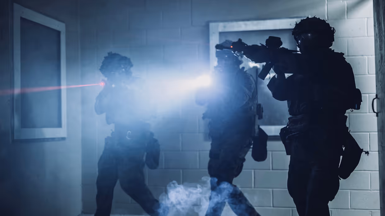 Drie mariniers die hun laserdots gebruiken bij de instap van een slecht verlichte kamer. 