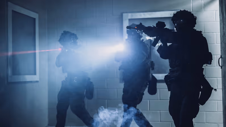 Drie mariniers die hun laserdots gebruiken bij de instap van een slecht verlichte kamer. 