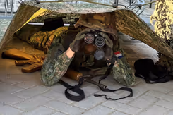 Militair met verrekijker onder tentdoek.