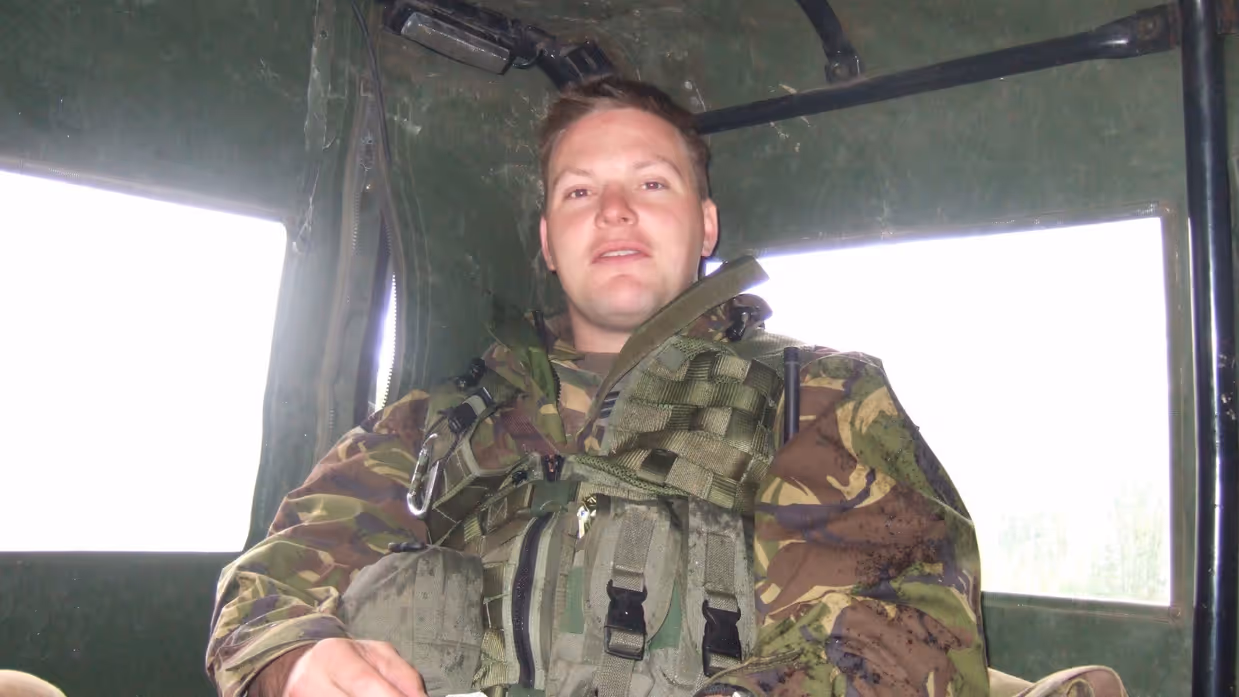 Een jonge Tim Nelissen in gevechtstenue zittend achterin in een militair voertuig. Hij kijkt in de camera.