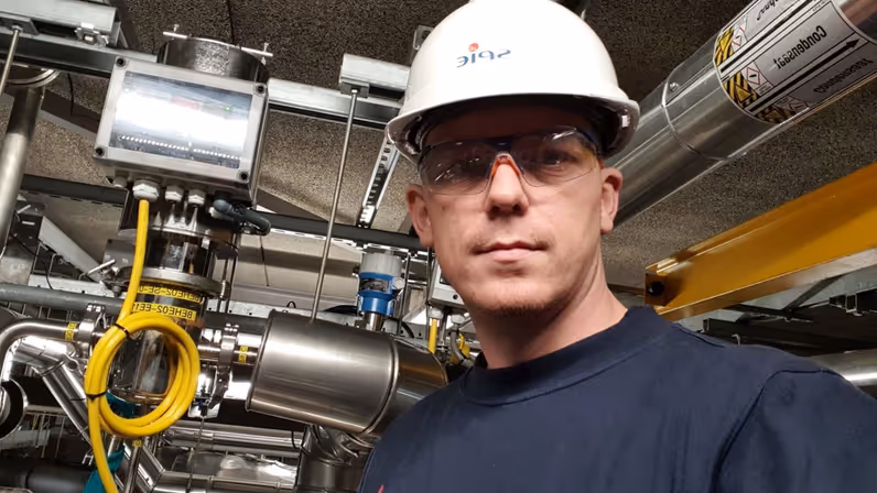 Glenn Afman met een witte helm en veiligheidsbril op vlak naast het binnenwerk van een machine.