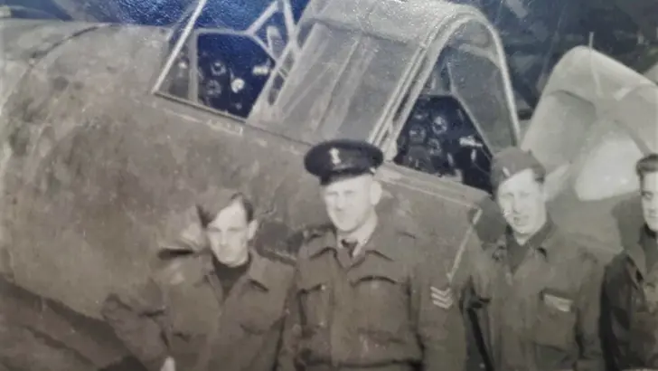 4 militairen op een zwart-wit foto poseren voor een oud vliegtuig.