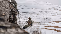 2 militairen die een rots beklimmen in een sneeuwachtig gebied.