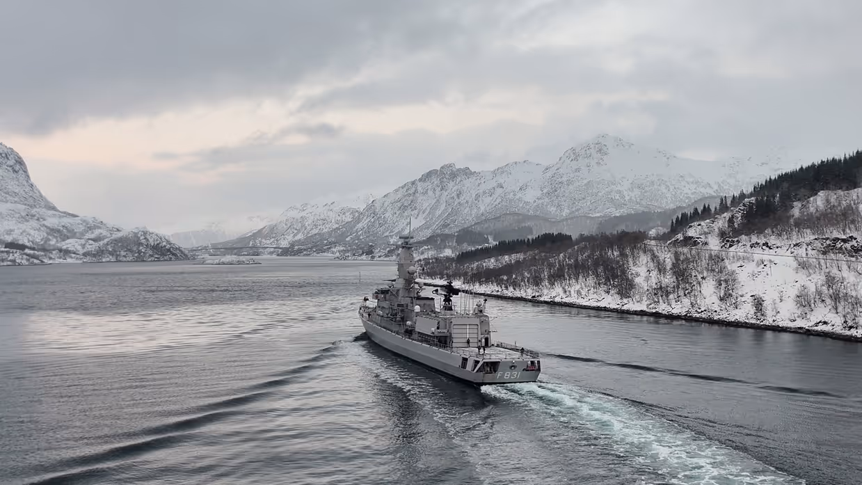 Militair schip vaart langs kust richting bergen.