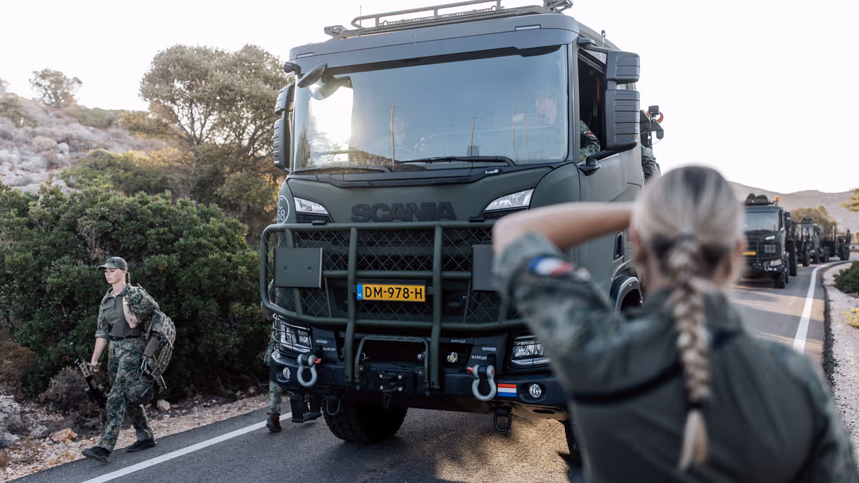Militairen houden toezicht en begeleiden een vrachtwagen.