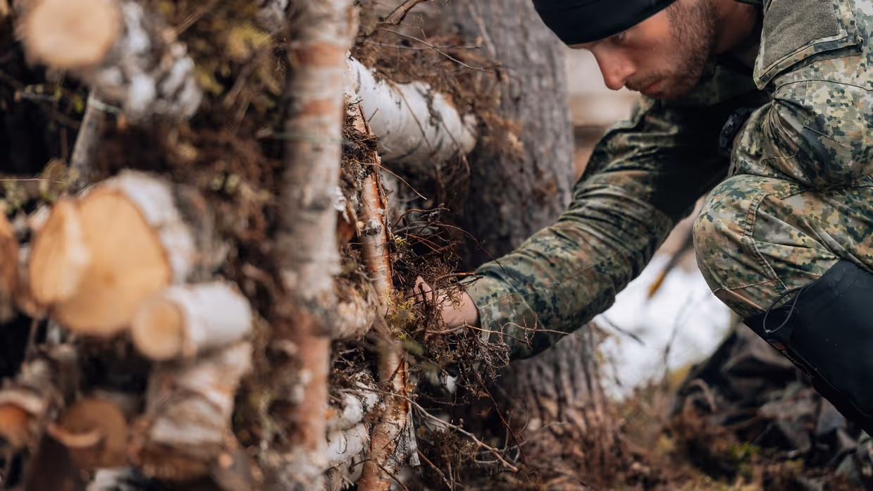 Een militair kijkt aandachtig naar een constructie van hout