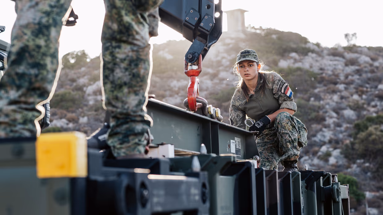 Twee militairen zijn cargo aan het verplaatsen met een kraan.