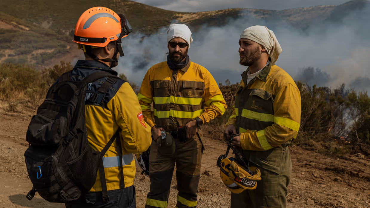 Drie medewerkers overleggen met elkaar met een bosbrand in de achtergrond