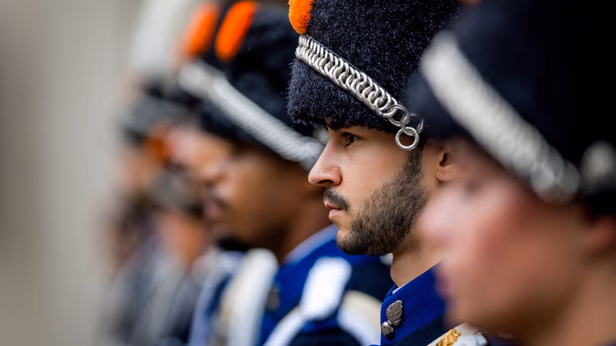 Een militair in ceremonieel ornaat staat naast zijn collega's.