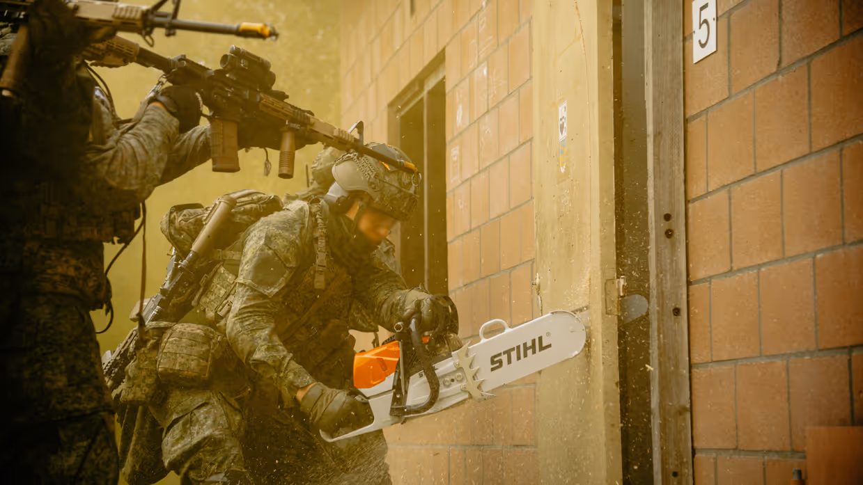 Militairen houden zicht terwijl een collega een deur benadert met een elektrische zaag.