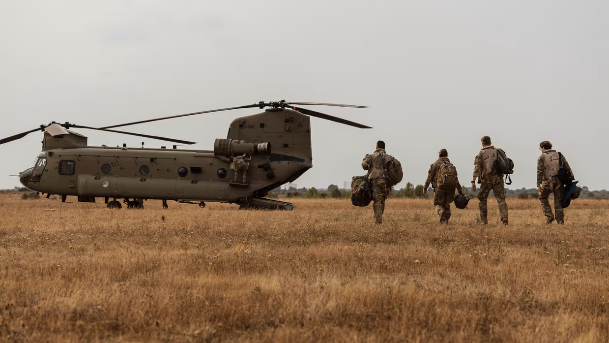 Vier militairen lopen met spullen naar een helikopter