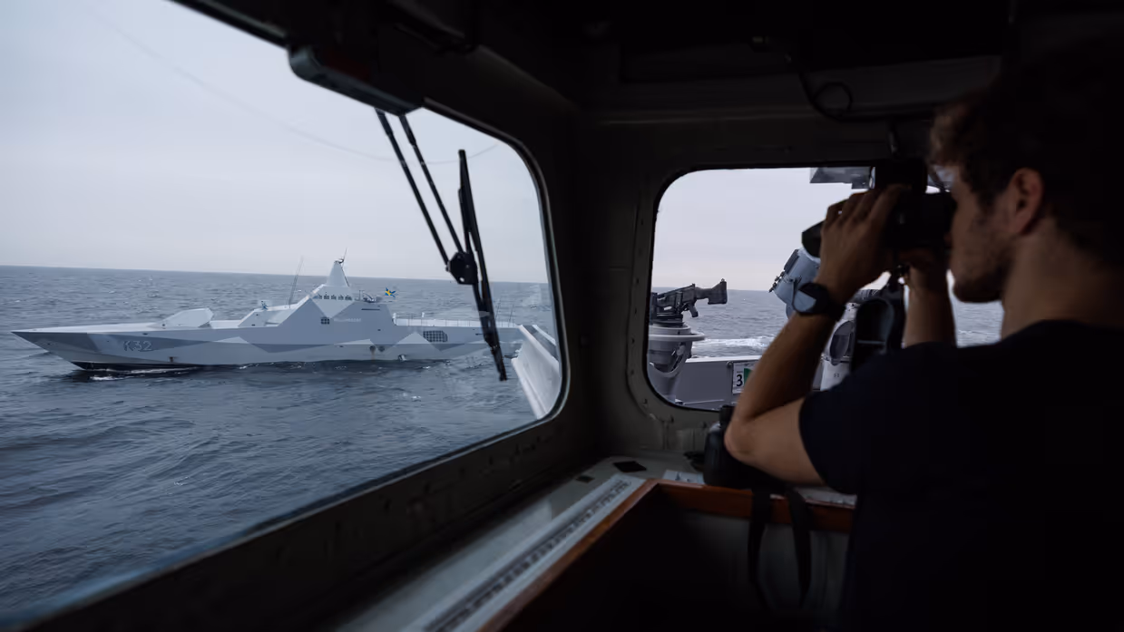 Een militair kijkt met een verrekijker toe op een ander schip.