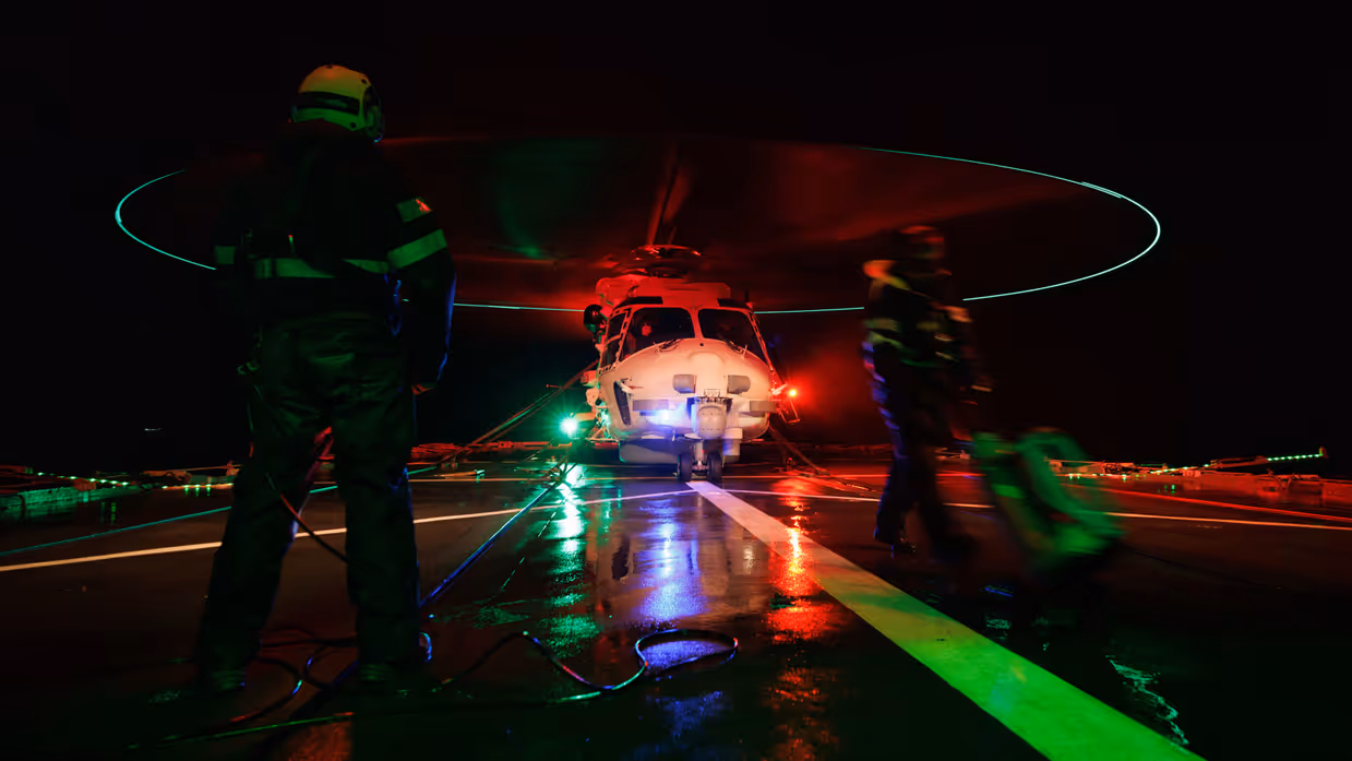Twee medewerkers maken een helikopter klaar voor vertrekt in de nacht.