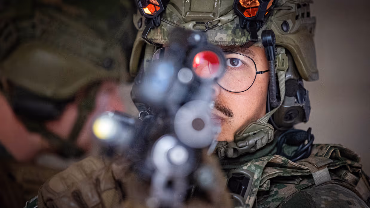 Een close-up van een militair met zijn geweer in de voorgrond.