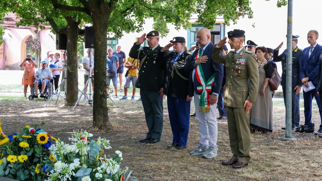 Militairen in uniform salueren en een man in pak met sjerp bij een krans.