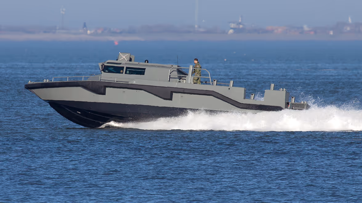 Een kleine grijze boot met twee man aan boord gaat met hoge snelheid over het rustige water.