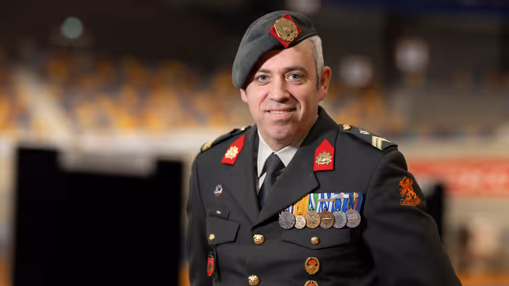 Militair met baret op en borst vol medailles kijkt lachend in camera. 