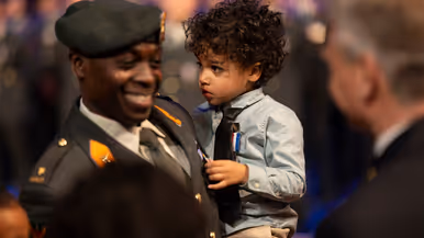 Kinderen van militair krijgen kindermedaille uitgereikt. Militair in uniform kijkt lachend in camera. 