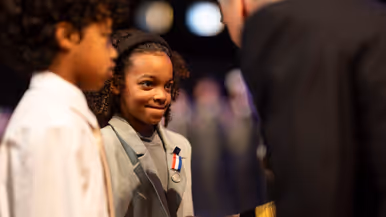Kinderen van militair krijgen kindermedaille uitgereikt. Militair in uniform kijkt lachend in camera. 